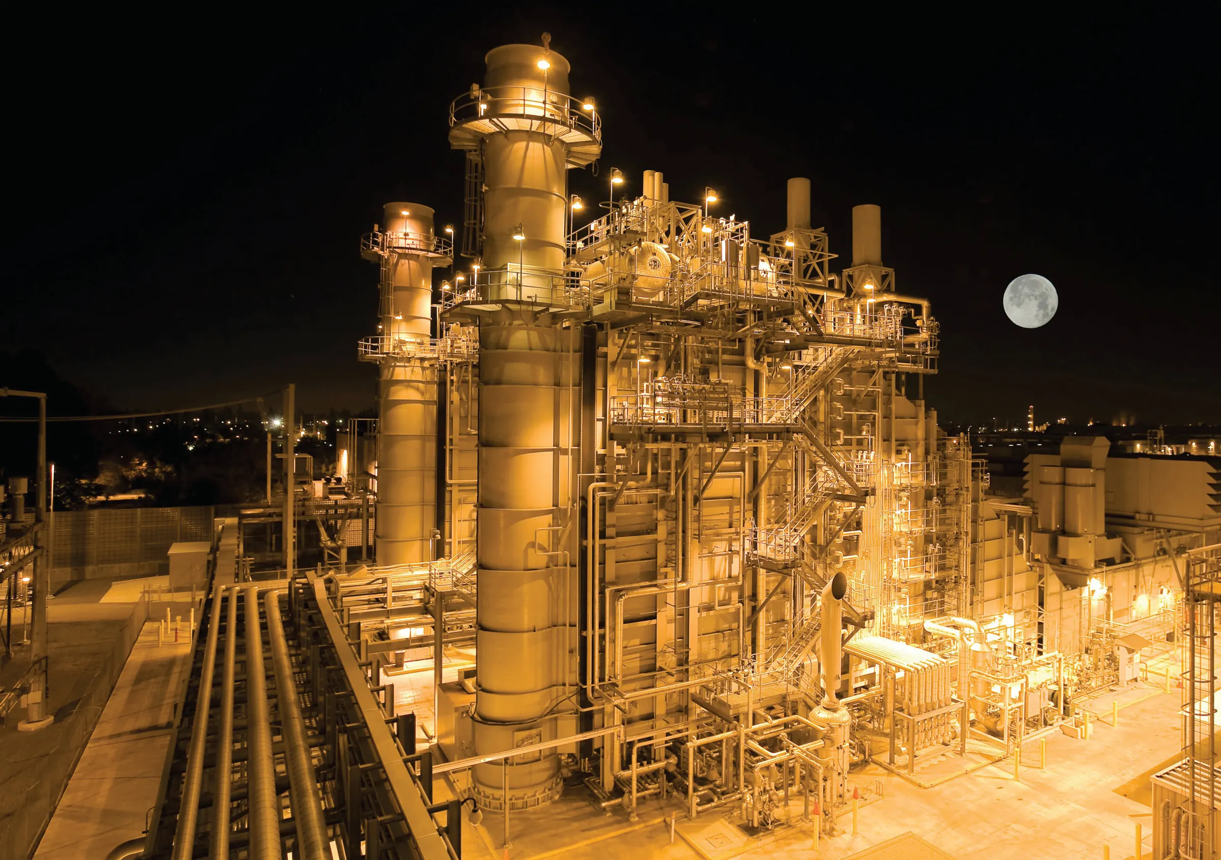 A power plant glowing at night under a full moon